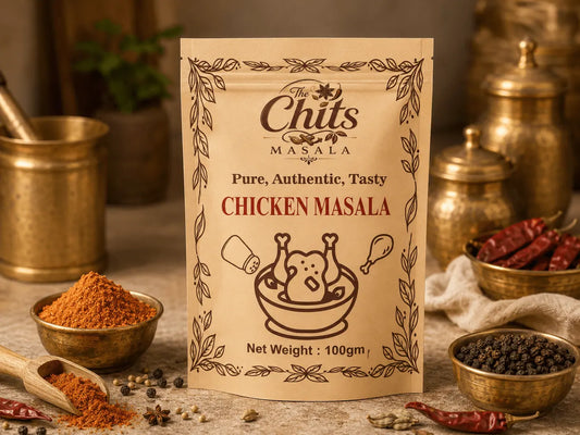 A 100g pouch of 'The Chits' Masala Chicken Masala spice mix, displayed in a rustic kitchen setting with brass bowls of spices, dried red chilies, and peppercorns.