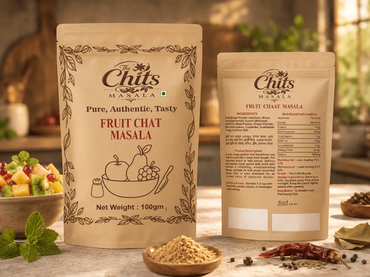 Two stand-up pouches of The Chits Masala Fruit Chat Masala displayed on a rustic wooden table with ingredients like dried red chilies, peppercorns, and mint leaves in the foreground.