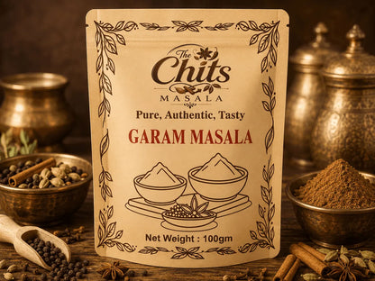A 100g pouch of 'The Chits Masala' Garam Masala spice mix, displayed on a rustic wooden table surrounded by spices, copper pots, and a wooden spoon.