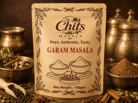A 100g pouch of 'The Chits Masala' Garam Masala spice mix, displayed on a rustic wooden table surrounded by spices, copper pots, and a wooden spoon.