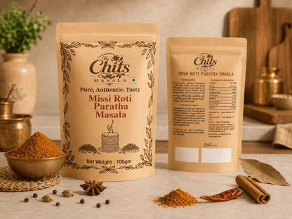 Two stand-up pouches of Chits Masala Missi Roti Paratha Masala displayed on a kitchen counter with spices, dried chilies, cinnamon sticks, and a leaf, with a blurred kitchen background.