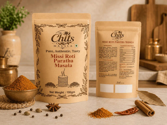 Two stand-up pouches of Chits Masala Missi Roti Paratha Masala displayed on a kitchen counter with spices, dried chilies, cinnamon sticks, and a leaf, with a blurred kitchen background.