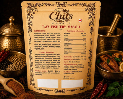 A stand-up pouch of Tava Fish Fry Masala by The Chits Masala, displayed on a wooden surface with spices and kitchen props around it. The front of the package is tan with black text and decorative border illustrations, and the back shows ingredients and nutritional information in English and Hindi.